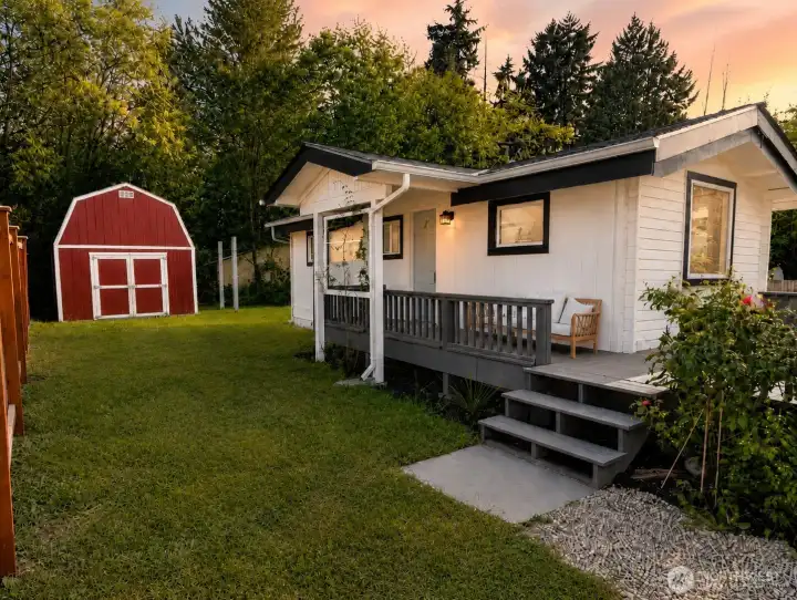 A charming exterior setting welcomes you with a spacious deck, peaceful yard, and a detached red storage shed that adds both character and function. The deck offers a great spot to relax, entertain, or enjoy the surrounding greenery, while the wide gravel path provides easy access through the yard. Mature trees create a private, cottage-like feel, and the generous outdoor space offers room for gardening, play, pets, or future outdoor living ideas.