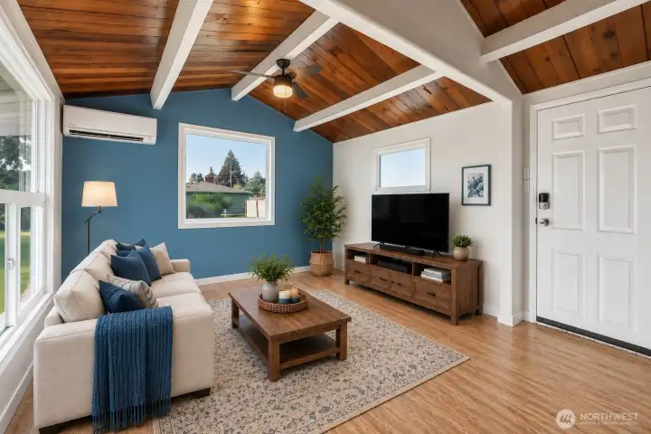 This open living area immediately captures attention with its soaring cedar ceiling and bold white beams, creating dramatic architectural character and warmth the moment you step inside. The spacious layout offers wonderful flexibility for living, dining, or entertaining. A ductless heat pump mini-split in the living room provides efficient heating and cooling for year-round comfort. With natural light, open flow, and unforgettable ceiling detail, this space offers a beautiful blend of charm, function, and everyday comfort.