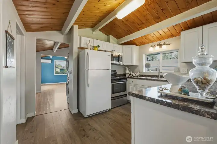This beautifully updated kitchen combines timeless character with everyday functionality, highlighted by soaring vaulted cedar ceilings with exposed beams that create warmth and architectural charm. Crisp white cabinetry, abundant counter space, and rich flooring provide a clean and inviting feel, while the large windows bring in natural light and backyard views. The efficient layout offers excellent flow for cooking and entertaining, blending modern updates with the home’s cozy Craftsman-inspired personality.