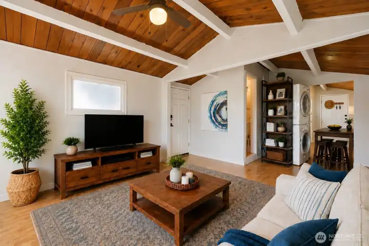 This inviting living/dining space features a beautiful cedar ceiling with striking white beams, adding warmth, character, and architectural charm. Large windows bring in natural light and peaceful greenery, while the open flow into the dining spot creates a comfortable setting for everyday living and entertaining. The warm wood tones make the space feel cozy, bright, and welcoming.