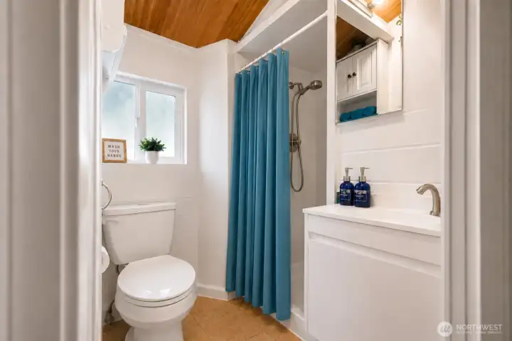 Bright and refreshed bathroom featuring crisp white finishes, updated vanity, modern fixtures, and charming cedar ceilings that add warmth and character. The clean, neutral design is complemented by natural light, built-in storage, and stylish blue accents, creating a fresh and inviting space perfect for everyday comfort.