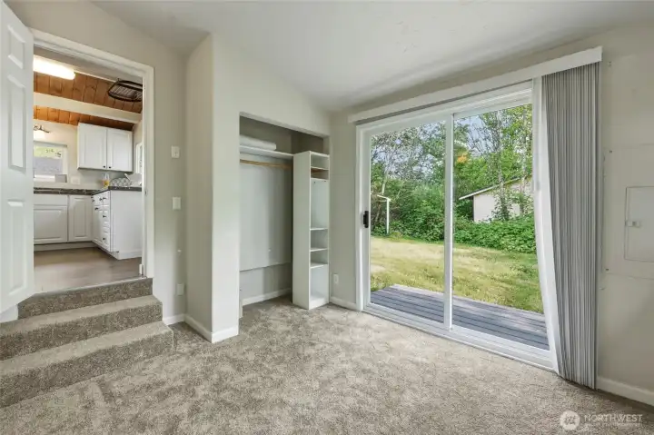 This bright and spacious bedroom offers a peaceful retreat with plush neutral new carpeting, generous proportions, and an abundance of natural light. The highlight is the large sliding glass door that opens directly onto a private wooden deck overlooking the lush, tree-filled backyard — perfect for morning coffee or evening relaxation. The open layout and high ceilings create an airy, inviting atmosphere. Conveniently located just steps from the kitchen via a short staircase, this bedroom blends comfort, functionality, and seamless indoor-outdoor living.