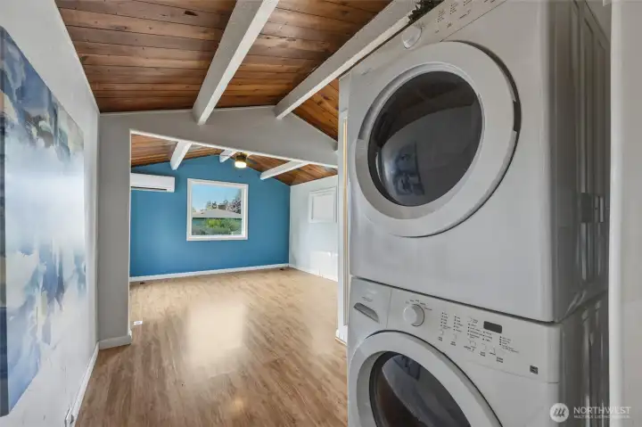 Conveniently located just off the living space, this bright and highly functional laundry area features a full-size stacked front-loading washer and dryer that make laundry day effortless. The space is enhanced by the home’s signature soaring vaulted tongue-and-groove wood ceilings with dramatic white beams, light wood-look flooring, and an open, airy feel that keeps it from feeling like a typical utility room. With excellent lighting, thoughtful layout, and seamless connection to the main living areas, this practical space adds everyday convenience while maintaining the warm, inviting character of the home.