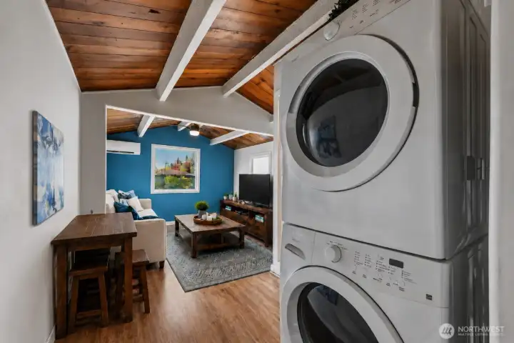 A thoughtfully designed layout blends character and functionality, featuring soaring vaulted cedar ceilings with exposed beams, durable flooring, and an open, airy feel throughout. The conveniently located full-size stacked washer and dryer maximize space efficiency while maintaining a clean modern look. The adjoining room showcases abundant natural light, a striking accent wall, and a ductless mini-split system for year-round comfort, creating a flexible space ideal for relaxing, working, or entertaining.