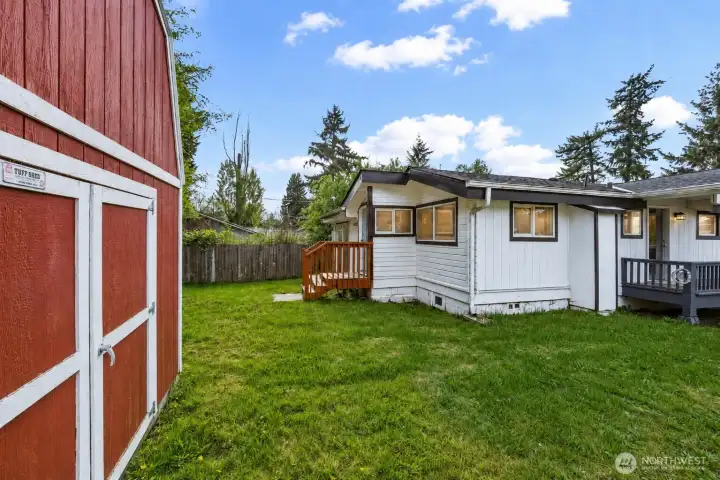 This expansive, sun-drenched backyard is a true highlight of the property, featuring a generous level lawn perfect for gardening, play, entertaining, or simply relaxing under the open sky. The standout feature is the large, classic red barn-style storage shed with double doors, offering exceptional utility and storage space for tools, equipment, or hobbies. A convenient wooden deck with stairs extends from the home, creating seamless indoor-outdoor living, while mature trees and fencing provide natural privacy and charm. Peaceful, functional, and full of potential, this inviting backyard is an ideal extension of the home’s living space.