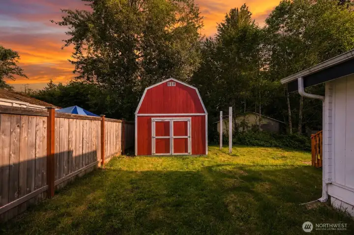 Tucked proudly in the backyard stands this impressive red barn-style storage shed — a true standout feature that offers incredible versatility and storage. With its classic gambrel roof and striking red exterior with white trim, it commands attention while blending beautifully with the lush, tree-lined setting. Inside, the generously sized, fully finished interior boasts high vaulted ceilings, OSB-paneled walls, a convenient built-in workbench, electrical outlets, and excellent lighting. Two lofted storage areas maximize vertical space, making it perfect for tools, seasonal items, a workshop, hobby room, or extra storage. Double doors provide easy access for larger equipment, and the thoughtful layout ensures this shed delivers exceptional functionality and value for years to come.