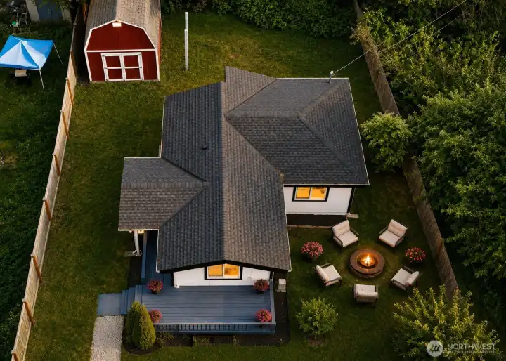 Aerial view highlights the generous outdoor space surrounding the home, with mature trees, open lawn areas, and a peaceful green setting. The property offers a large private yard with room to garden, play, relax, or create inviting outdoor living spaces. The deck adds a welcoming spot for morning coffee or summer seating, while the large red storage shed provides excellent functionality for tools, equipment, hobbies, or seasonal storage. With a blend of open space, natural privacy, and practical outdoor features, this property offers room to breathe, room to gather, and room to enjoy the beauty of the outdoors.