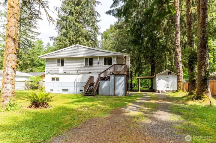 Front approach. Gravel driveway with room for boats, trailers, and multiple vehicles. Detached shop/carport visible at right.