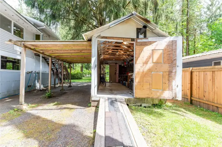 Detached shop with attached carport and wood stove inside, covered parking outside, and enough room for a motorcycle, tools, and gear.