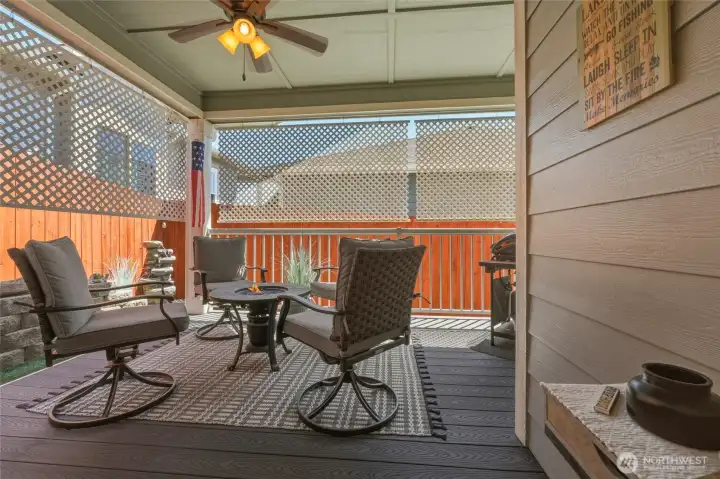 Covered outdoor living area with ceiling fan, privacy lattice, and fire table for year-round enjoyment.
