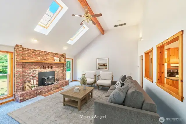 Natural light pours into this open living area, showcasing the vaulted ceilings and classic brick fireplace (virtually staged).