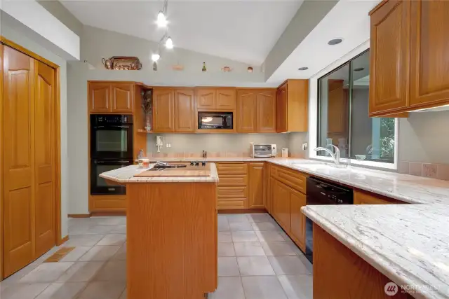 The kitchen features vaulted ceilings, rich wood cabinets, granite countertops, a functional island, and a spacious pantry—designed for both style and practicality.