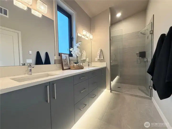 Primary en suite with motion activated under cabinet lighting, dual vanity, full glass and tile shower.