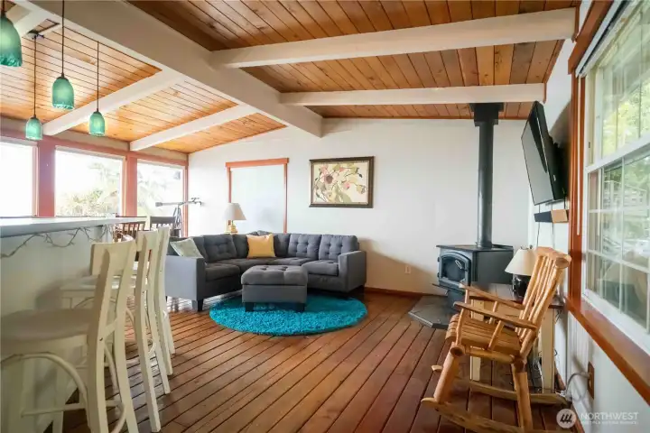 Living room has beautiful vaulted ceiling with exposed beams & tongue & groove wood floors with wood burning stove. The dining room has a wall of windows with incredible Southerly view.