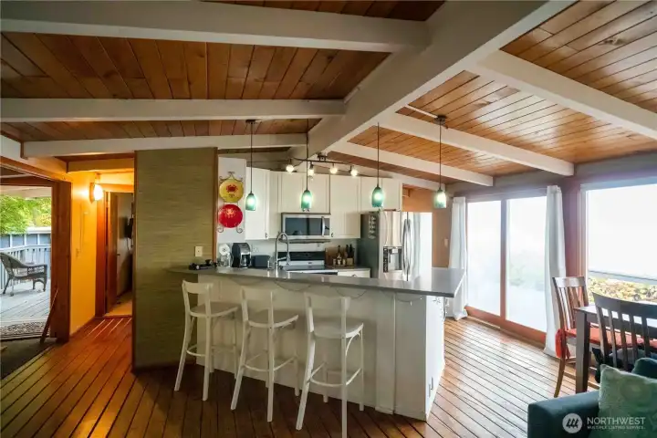 Open concept living area offers beautiful vaulted ceiling with exposed beams & tongue & groove wood floors with wood burning stove. The dining room has a wall of windows with incredible Southerly view. Kitchen has wrap around quartz eating.