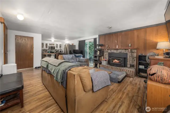 Unit 1 Spacious living area featuring wood-style flooring, a brick fireplace insert, and wide open-concept flow into the kitchen and dining spaces — ideal for flexible layouts and everyday comfort.