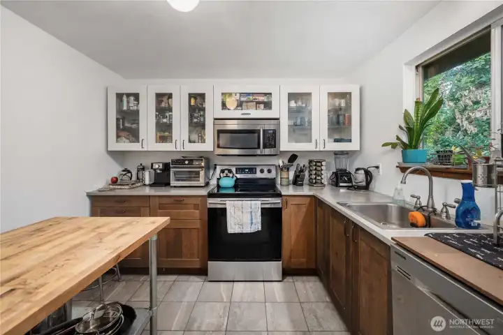 Unit 1 Spacious U-shaped layout offering ample counter space, overhead cabinetry, and a smooth-top electric range with built-in microwave above for convenience.