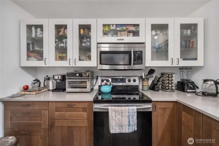 Unit 1 Stainless range and microwave surrounded by updated shaker cabinets, showcasing generous storage and functional prep space for cooking and daily living.