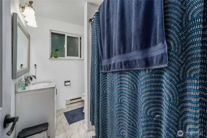 Unit 1 Bright and practical full bathroom featuring easy-care tile flooring, a shower/tub combo, and updated lighting. Neutral finishes make it simple to personalize, and a large window helps keep the space light and fresh.