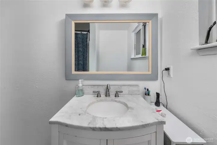 Unit 1 A modern vanity with a marble-style countertop provides storage and a clean, updated look. The oversized framed mirror and contemporary fixtures add a polished touch to the space.