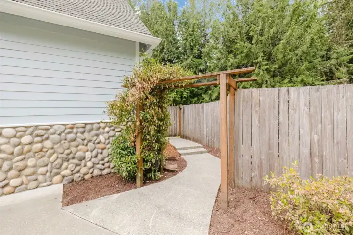 Sidewalk leading from the driveway around to the backyard is crowned with beautiful trellis.