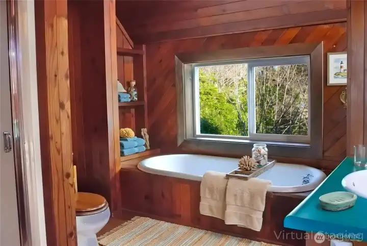 The upstairs bathroom features a warm wood-lined design with a soaking tub, built-in shelving, and a serene, spa-like atmosphere.