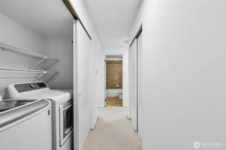 In-unit laundry area with shelving and additional hallway storage.