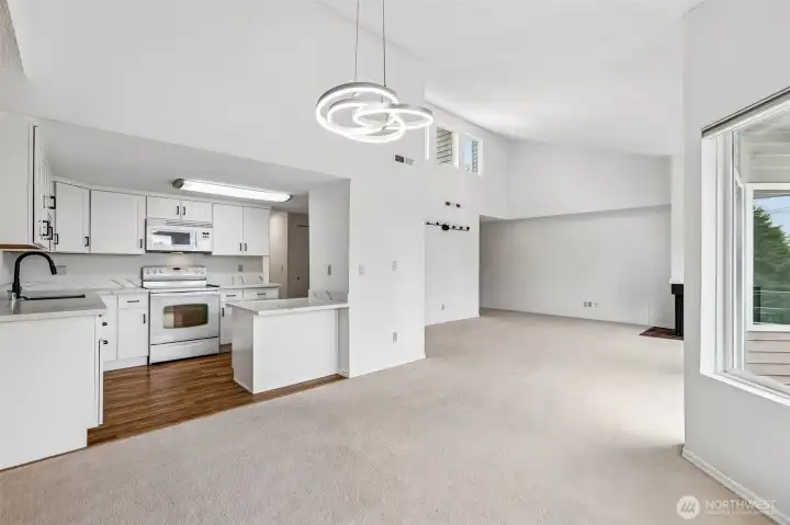 Open living and dining area with vaulted ceiling, fireplace, and balcony access.