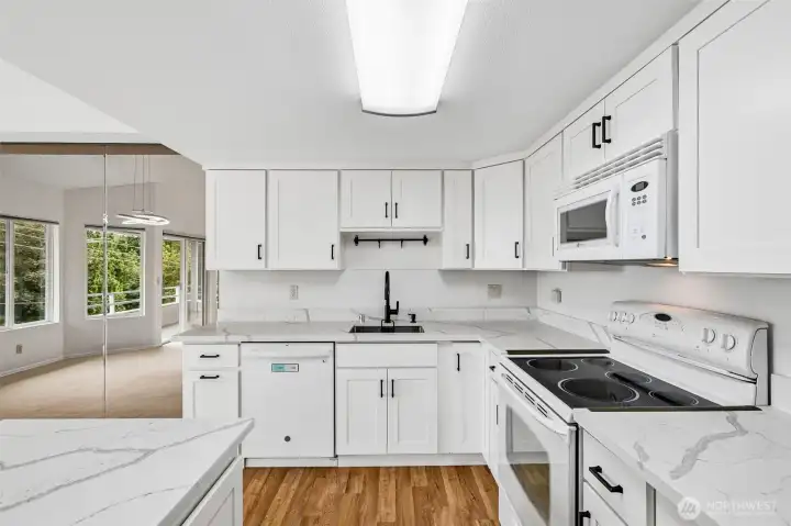 Updated kitchen with white cabinetry, quartz-style counters, breakfast bar, and wood-look flooring.