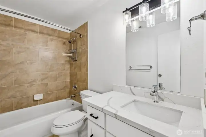 Full bathroom with tiled tub/shower surround, updated vanity, and modern lighting.