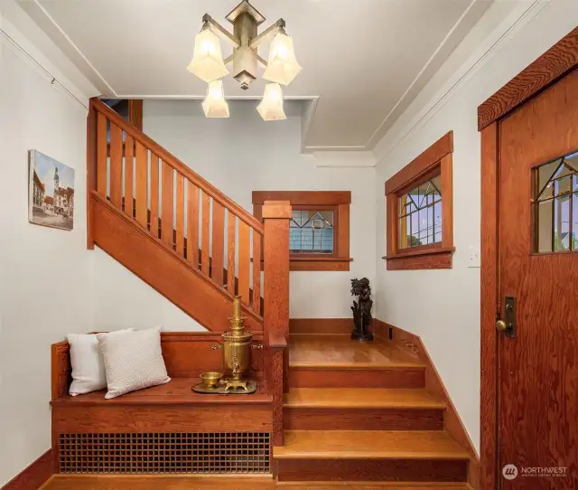 The foyer is the perfect introduction to the rest of the home with its old growth fir built-in bench with storage below it, railing and leaded windows.