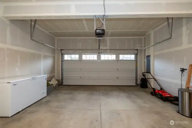 Large garage that includes shelves, lawn mainenance items, and large chest freezer.