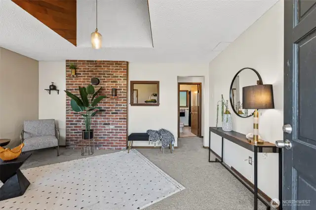 Step into a bright and inviting living room featuring soaring high ceilings and a striking brick accent wall that adds warmth and character.
