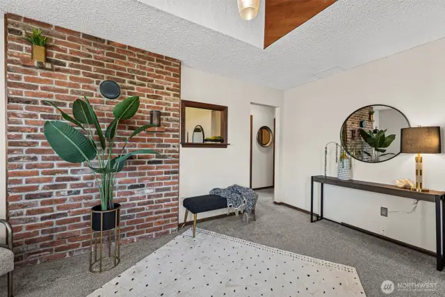 The living room welcomes you with cozy carpet, soaring ceilings, and a beautiful brick accent wall, creating a warm and inviting atmosphere.