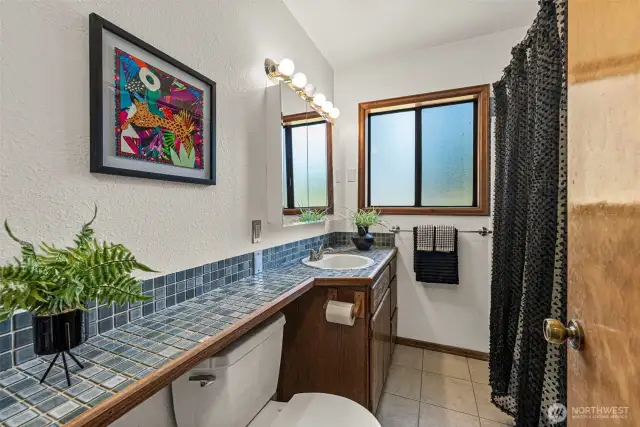 The full bath has everything you need, featuring a functional layout with a combination tub and shower, a spacious tiled vanity, and storage for essentials.