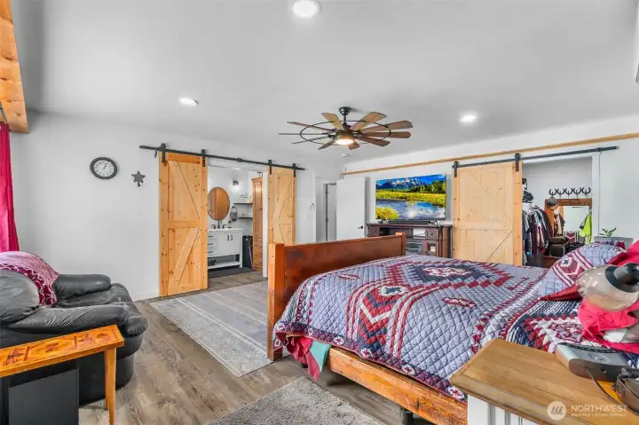 Another view of the primary bedroom downstairs and the walk-in closet as well as the adjoining bathroom. Canned lighting as well as a ceiling fan with light. More wood shelving around the room for pictures.