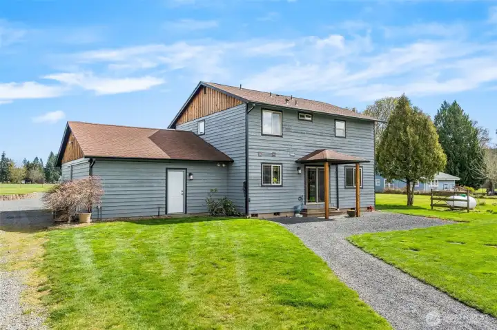 This view is of the back of the home. White door is entrance to the mud room. Slider enters to dining area. Large covered area to the back of house. Large backyard  with trees including mature Japanese Maple.