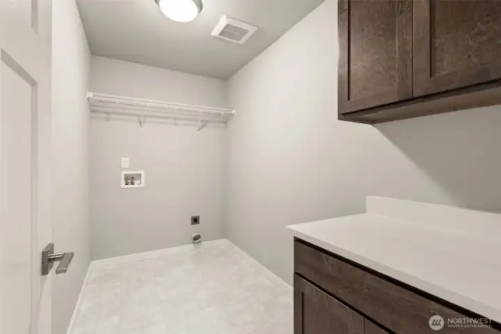 Separate laundry room with a counter, storage cabinets and a storage shelf above appliances.