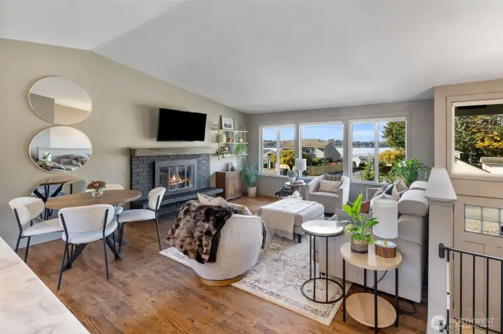 Living room with vaulted ceiling, hardwood floors, wood burning fireplace and wall of windows providing breathtaking views of Lake Stevens