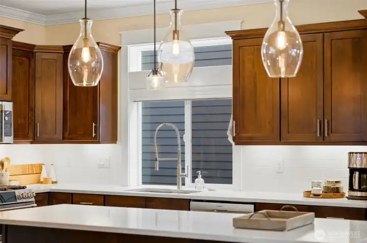 Designer pendant lighting and quartz counters frame the kitchen window — craftsman details throughout. Designer pendant lighting and quartz counters frame the kitchen window — craftsman details throughout.