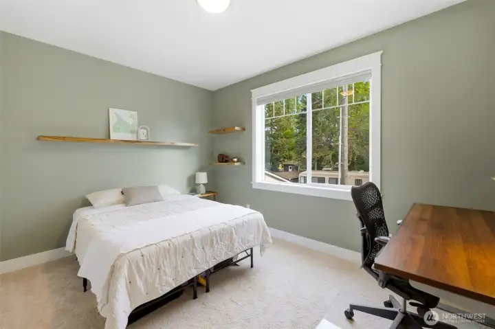 Bright bedroom with sage walls, floating shelves, and treetop views — flexible for guests, office, or nursery. Bright bedroom with sage walls, floating shelves, and treetop views — flexible for guests, office, or nursery.