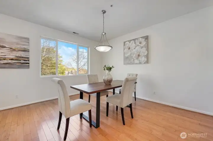 Dining room features large windows that fill the space with natural light and offer serene views of the surrounding trees and distant mountains. The room is elegantly simple, with warm hardwood floors, soft neutral walls, and tasteful artwork adding character without overwhelming the space. A modern light fixture centers above a sleek wooden dining table surrounded by four upholstered chairs, creating a welcoming atmosphere perfect for everyday meals or intimate gatherings. The mountain views provide a tranquil backdrop, enhancing the room’s natural beauty and sense of openness.