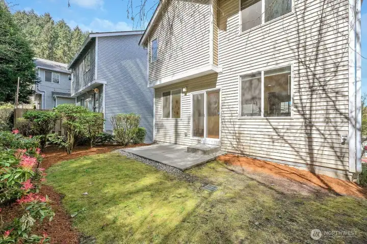 Private backyard features fresh mulch, tidy landscaping, and a clean, low-maintenance layout perfect for outdoor relaxation. A cozy patio extends from the home, offering space for seating or grilling, while surrounding greenery and mature trees create a peaceful, natural backdrop. It’s an inviting outdoor retreat with room to enjoy everyday living.