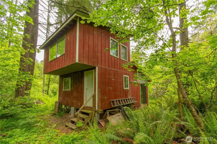 This view of the cabin is from the side and back of the cabin. Upper bedroom floor hangs over the side of the cabin. Also view of the back of the home with sliding door off the living room.