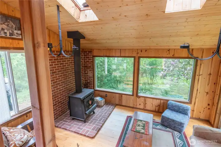 A few steps down to the living room with large windows to let in the natural light. Free standing wood stove for heat.  Propane run lights. Natural wood ceiling with brick hearth and brick behind the free standing wood stove.