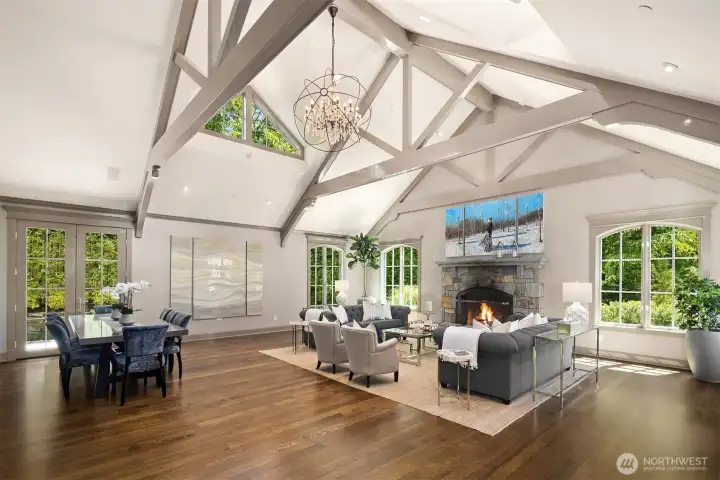 Dramatic living room featuring soaring vaulted ceilings with painted beams and a statement contemporary chandelier. The focal point is a massive, stone-surround wood-burning fireplace. Rich hardwood floors and elegant French doors open directly to the lush outdoors. Dramatic living room featuring soaring vaulted ceilings with painted beams and a statement contemporary chandelier. The focal point is a massive, stone-surround wood-burning fireplace. Rich hardwood floors and elegant French doors open directly to the lush outdoors.