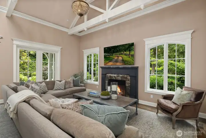 A closer look at the family room's inviting lounge area, showcasing the dramatic scale of the soaring vaulted ceilings accented by painted architectural beams. Expansive windows frame bright views of the lush exterior greenery, while a handsome fireplace serves as the cozy centerpiece for this comfortable, sun-drenched gathering space. A closer look at the family room's inviting lounge area, showcasing the dramatic scale of the soaring vaulted ceilings accented by painted architectural beams. Expansive windows frame bright views of the lush exterior greenery, while a handsome fireplace serves as the cozy centerpiece for this comfortable, sun-drenched gathering space.