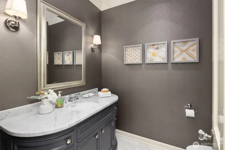 Perfectly positioned for guests, the main floor powder room is a chic and sophisticated space. It features rich wall treatments complemented by classic sconce lighting, a handsome dark-toned vanity with a premium marble countertop, and elegant polished fixtures that add a touch of timeless luxury. Perfectly positioned for guests, the main floor powder room is a chic and sophisticated space. It features rich wall treatments complemented by classic sconce lighting, a handsome dark-toned vanity with a premium marble countertop, and elegant polished fixtures that add a touch of timeless luxury.
