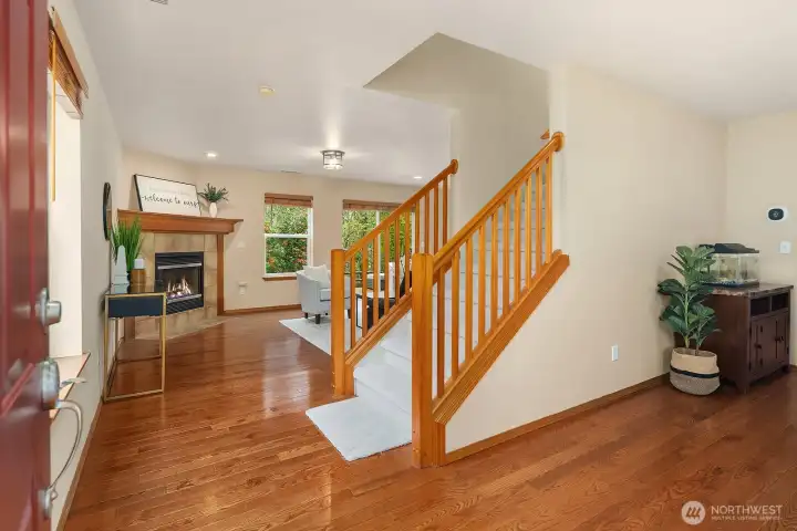 This bright and welcoming entry showcases beautiful hardwood floors that flow seamlessly throughout the main level, an elegant staircase with warm wood railings, and an open sightline straight into the inviting living areas beyond. The airy, light-filled space and thoughtful layout create an immediate sense of warmth and comfort the moment you step inside.