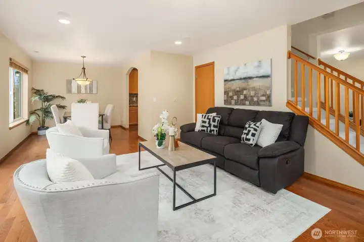 This inviting view captures the seamless connection between the living room and the rest of the main level, with gleaming hardwood floors, designer paint, and an open layout that flows effortlessly toward the kitchen and dining areas. The elegant staircase framing the background adds a lovely architectural touch while reinforcing the home's thoughtfully designed and cohesive interior.